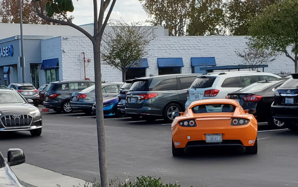 Original Tesla Roadster driving in parking lot.