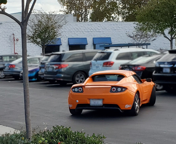 Original Tesla Roadster driving in parking lot.